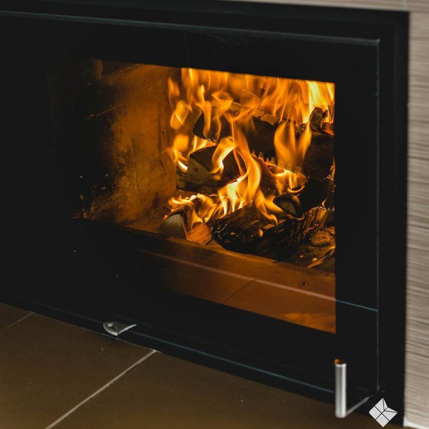 A modern fireplace with burning wood inside. The flames are bright and illuminating the inside of the fireplace.