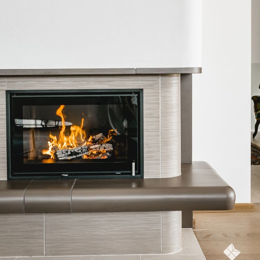 A modern fireplace with a black frame and a glass door is burning brightly, casting light on the room. The fireplace has a sleek design, and the flames are dancing inside.