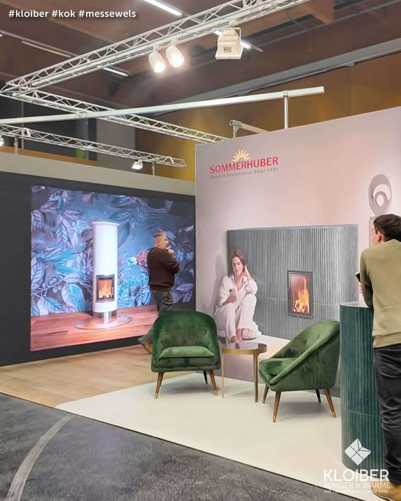 A display area with a projector screen showing a man speaking. There are two green chairs in front of a desk with a fireplace and a woman on the wall.