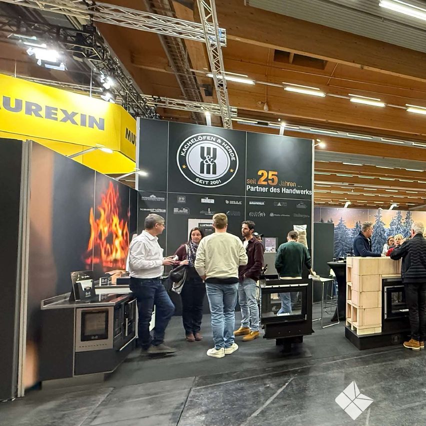 Several people stand in front of a booth at a trade show. They are discussing and looking at a fireplace. The booth has a yellow wall with a fire graphic.