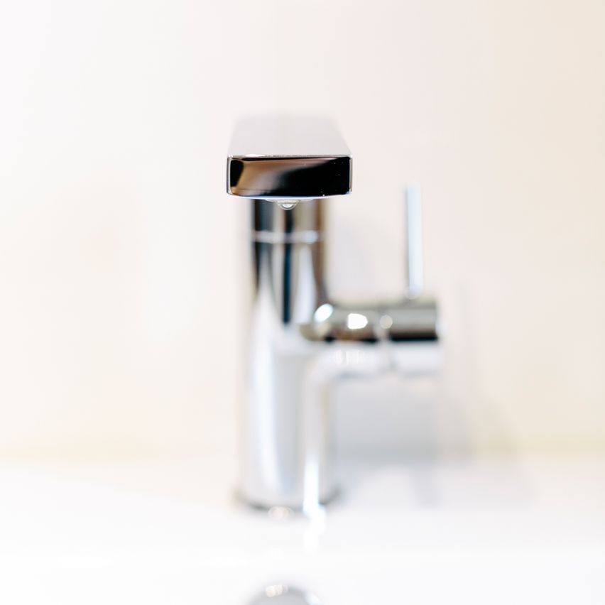 Eine Nahaufnahme eines modernen, edelstahlfarbenen Waschbecken-Wasserhahns mit einem einzelnen Griff und einer Wassertropfen, der vom Auslauf tropft.