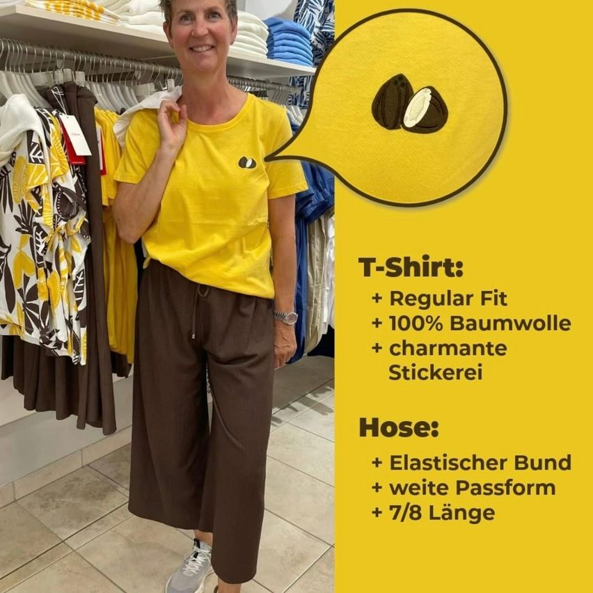 Eine Frau in einem gelben T-Shirt und braunen Hosen steht in einem Bekleidungsgeschäft. Eine Sprechblase hebt die Eigenschaften des T-Shirts hervor: Regular Fit, 100% Baumwolle und ein gesticktes Etikett.
