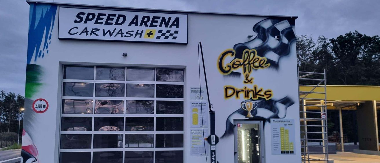 Das Äußere einer Speed Arena Autowäsche mit einem Wandbild von Kaffee & Getränken und einem Pokal an der Wand.