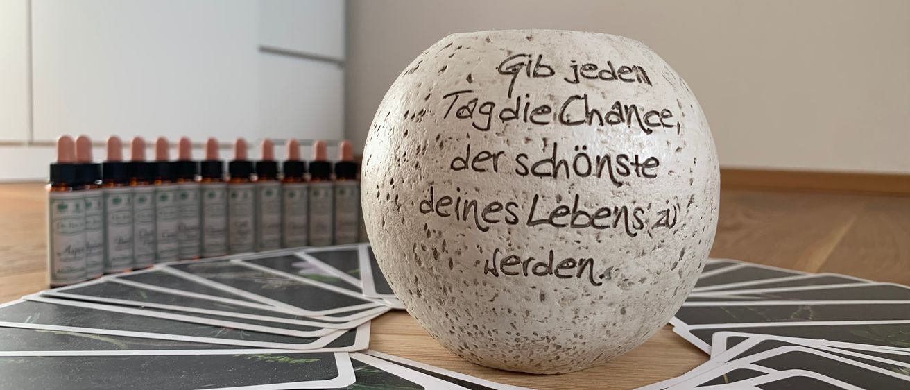 Ein kugelförmiges Objekt mit einer inspirierenden deutschen Zitat befindet sich auf einem mit Karten bedeckten Tisch. Das Zitat lautet: 'Gib jedem Tag die Chance, der schönste deines Lebens zu werden.'