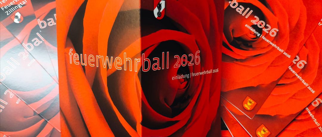 Eine rote Box zeigt 'Feuerwehrball 2026' mit einem Rosendesign. Sie liegt auf anderen ähnlichen roten Boxen, wahrscheinlich Einladungen.