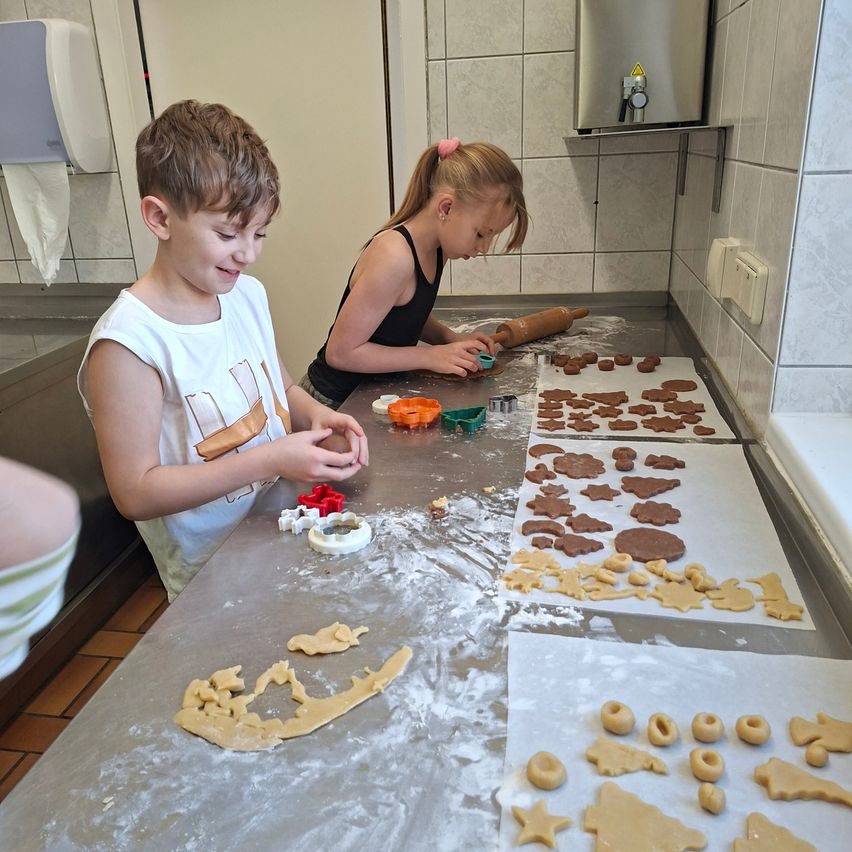Zwei Kinder backen Lebkuchen auf einem Küchentresen. Eines benutzt ein Nudelholz und das andere schneidet Formen aus.