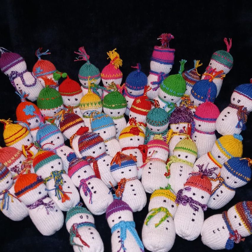 Eine Sammlung von gestrickten Schneemännern in verschiedenen Farben und Stilen, jeder mit einer anderen Mütze und einem Schal, in einem Kreismuster auf einem schwarzen Hintergrund angeordnet.