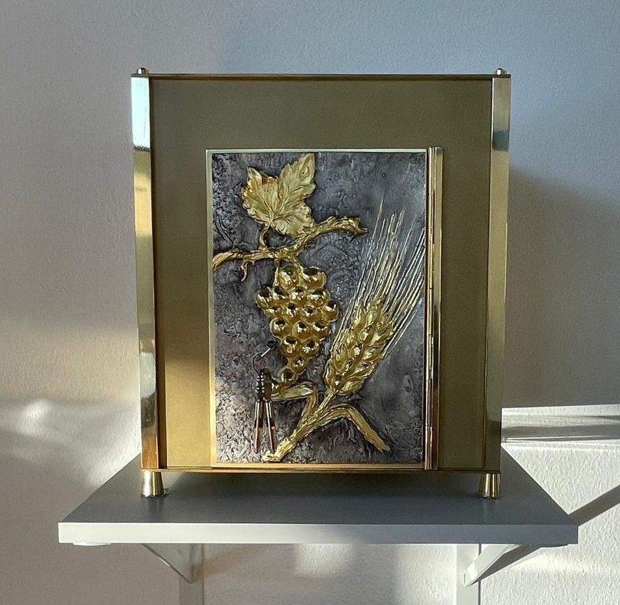 Ein Metallrahmen mit einem goldfarbenen Blatt- und Weizendesign auf einem weißen Regal an einer weißen Wand.