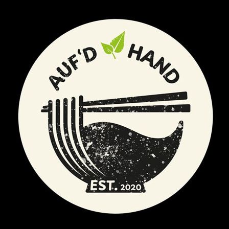 Ein kreisförmiges Logo mit den Worten 'AUF'D HAND' in weißer Schrift, über einer Schüssel mit Nudeln und Chopsticks. Unten steht die Schüssel, darunter steht 'EST. 2020'. Das Logo zeigt ein grünes Blatt auf der linken Seite.