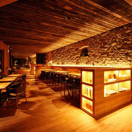 Ein Restaurant-Interieur mit Holztischen und Stühlen, einer Holzdecke und einer Steinmauer.