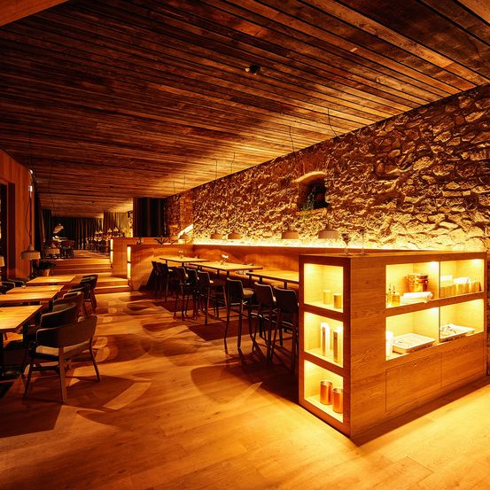 Ein Restaurant-Interieur mit Holztischen und Stühlen, einer Holzdecke und einer Steinmauer.