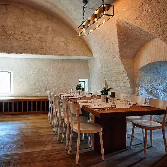 Ein großer Esszimmer mit Holzboden, weißen Wänden und einem langen Holztisch, der für eine Mahlzeit gedeckt ist.