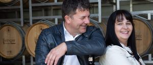 Ein Mann und eine Frau lächeln vor einer Reihe von Weinfässern mit der Aufschrift Leringer.