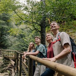 Ein Mann und eine Frau mit zwei Kindern stehen auf einer Holzbrücke im Wald. Sie alle lächeln und schauen in die Kamera.