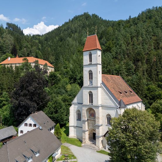 Luftaufnahme einer Kirche in den Bergen, ein Gebäude mit rotem Dach im Hintergrund.