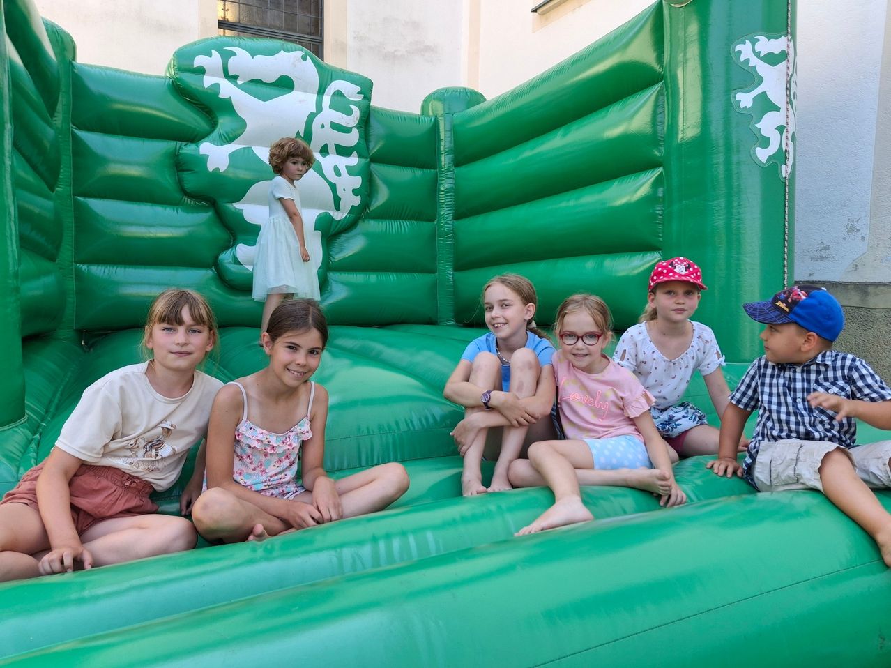 Eine Gruppe von Kindern sitzt auf einem aufblasbaren Drachen-Rutschvergnügen. Ein Mädchen steht dahinter und lächelt. Sie tragen alle Freizeitkleidung.