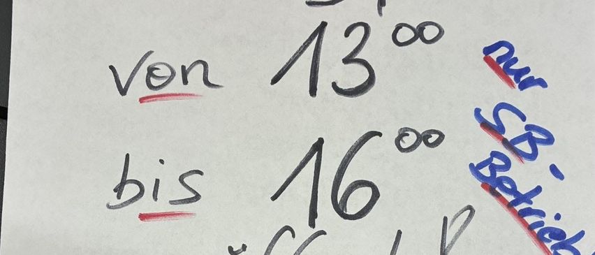 Ein weißes Papier mit einer handgeschriebenen Nachricht in schwarzer und roter Tinte. Es steht 'Sonntag, 21.12.' mit 'Von 13:00 bis 16:00 geöffnet?' und '-21%'. Es gibt eine rote Linie unter 'Sonntag' und eine rote Linie unter '21'.