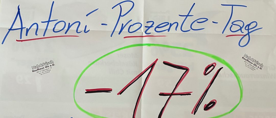 Ein weißes Papier zeigt handgeschriebenen Text: 'SA, 17.1.26 Antoni-Prozent-Tag -17% aus dem gesamten EINKAUF?' Es hat grüne und blaue Highlights.