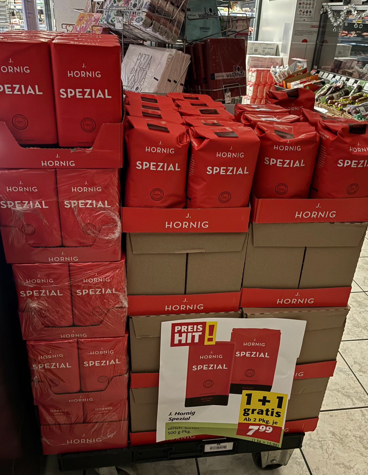 Eine Ausstellung von roten Hornig Spezial Kaffeebeuteln und -boxen in einem Geschäft. Die Beutel sind pyramidenförmig gestapelt. Ein weißes Schild zeigt eine Preisaktion an.