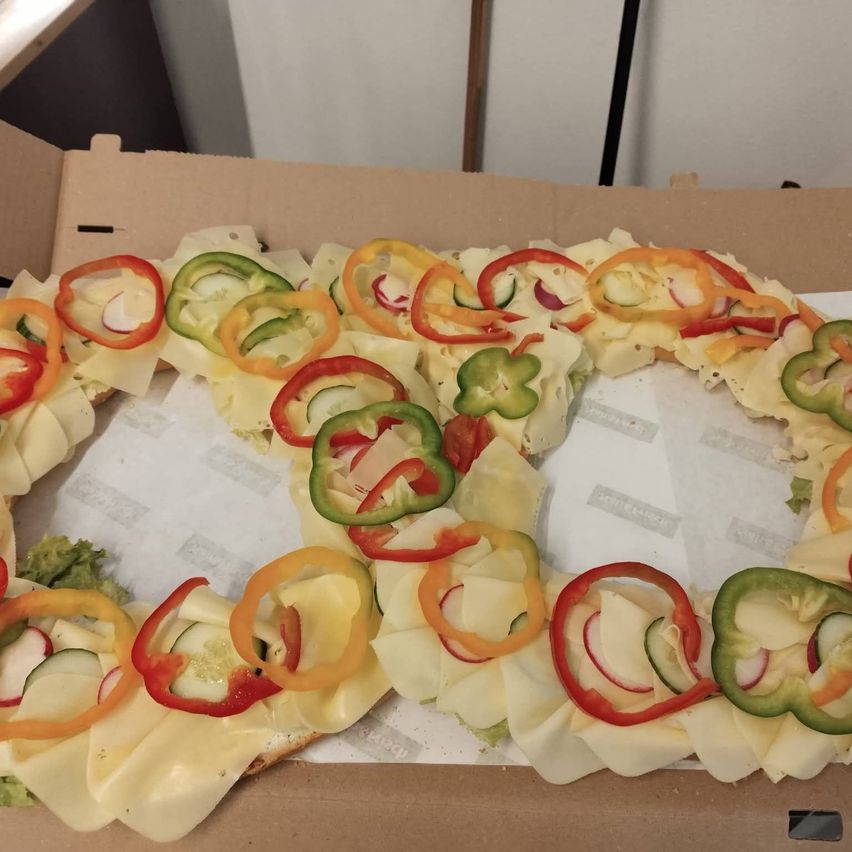 A pizza box with a circular arrangement of cheese and vegetable slices, including red, yellow, and green bell peppers, radishes, and cucumber. The pizza is topped with cheese and placed in a box.