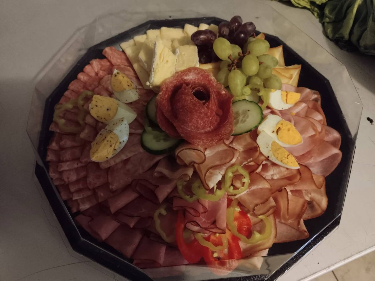 A charcuterie board with various meats, cheese, grapes, eggs, cucumbers, and peppers.