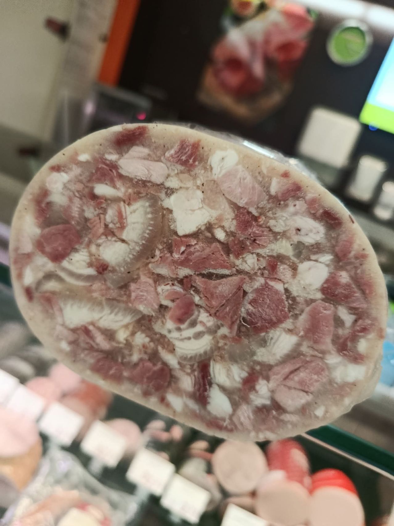 Eine Nahaufnahme eines Scheibes Salamiwurst mit sichtbaren Fleisch- und Fettstücken, wahrscheinlich auf einem Glasdisplay.