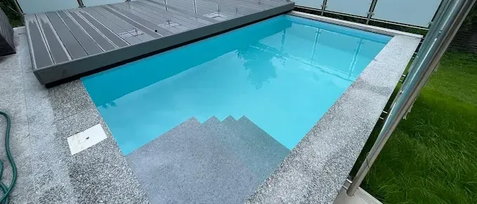 Ein leerer Pool mit Stufen und einer Abdeckung befindet sich auf einem Balkon, der von einem Metallzaun und einer Rasenfläche umgeben ist.