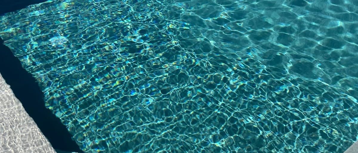 Ein Schwimmbecken mit klarem blauem Wasser und einer glatten Kante. Das Wasser zeigt sanfte Wellen und Lichtreflexionen.
