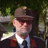 Ein Mann in Uniform mit Hut und Brille steht im Freien in der Nähe eines Baumes.