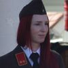 Eine Frau mit roten Haaren in einer Militäruniform mit schwarzem Hut und Krawatte. Sie schaut zur Seite.