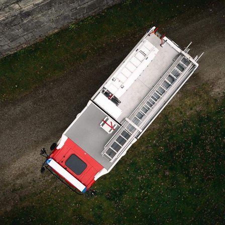 Ein Vogelperspektiveblick auf einen roten und weißen Feuerwehrwagen mit Leitern auf beiden Seiten und einer nahe gelegenen Ziegelmauer.