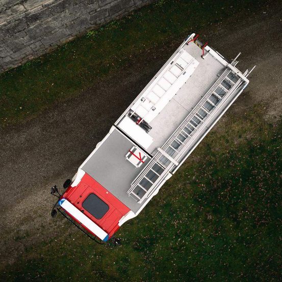 Ein Vogelperspektiveblick auf einen roten und weißen Feuerwehrwagen mit Leitern auf beiden Seiten und einer nahe gelegenen Ziegelmauer.