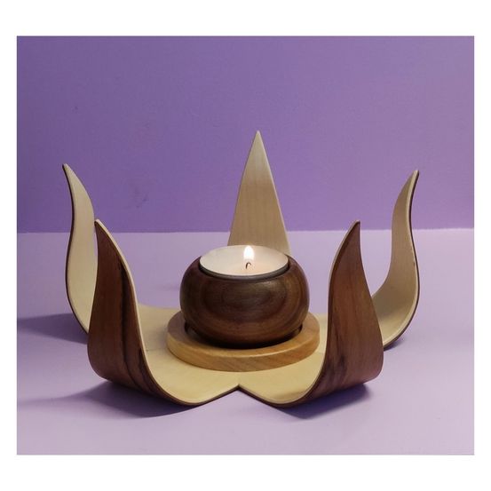 Ein hölzerner Kerzenhalter in Form einer Blume steht auf einer violetten Oberfläche. Die Kerze ist angezündet und wirft ein warmes Licht.