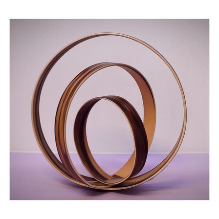 Drei kreisförmige Holzringe in Spiralform auf einer lila Oberfläche vor hellrosa Hintergrund gestapelt.