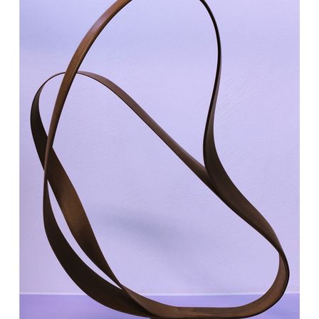 Eine bronzene Skulptur mit kurvigem, abstraktem Design steht vor einem lila Hintergrund. Die Skulptur besteht aus mehreren sich überschneidenden Bögen, die ein dynamisches und fließendes Erscheinungsbild erzeugen.