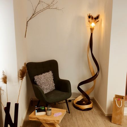 Eine gemütliche Ecke mit einem dunkelgrünen Stuhl, einem Holztisch und einer einzigartigen Holzlampe. Der Raum ist mit hellen Wänden und Holzboden ausgestattet.