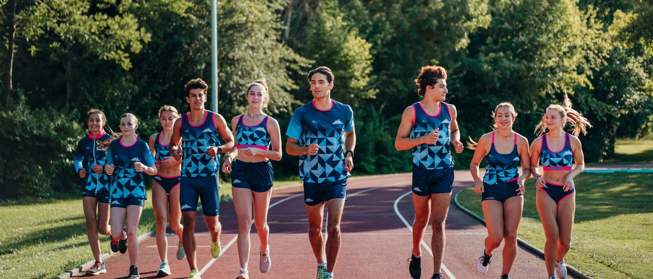 Eine Gruppe junger Athleten läuft auf einer Laufbahn in passenden blauen Uniformen. Der Hintergrund zeigt üppige grüne Bäume.