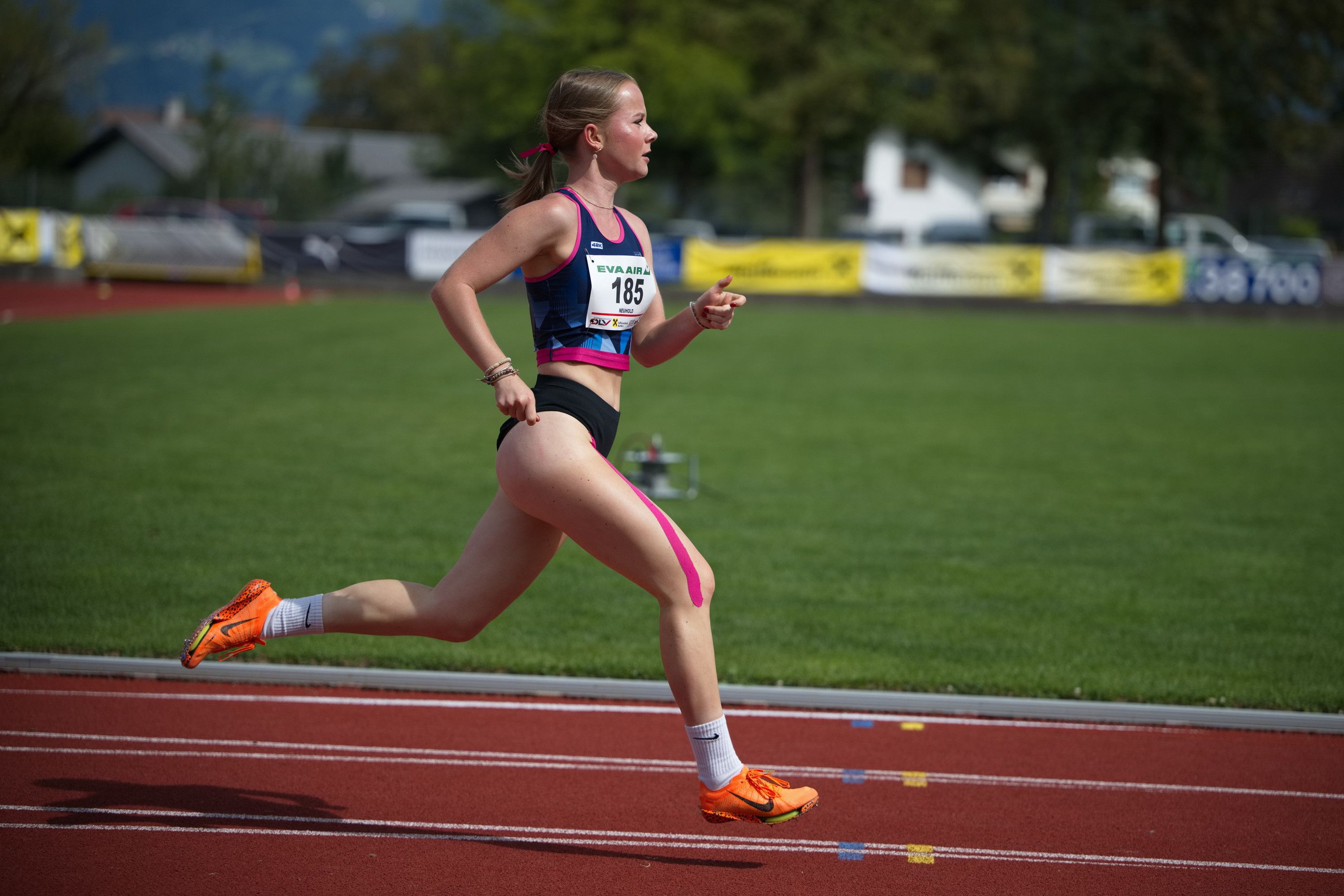 Eine weibliche Athletin mit der Nummer 185 läuft auf einer Laufbahn, trägt ein blaues und rosa Sporttrikot.