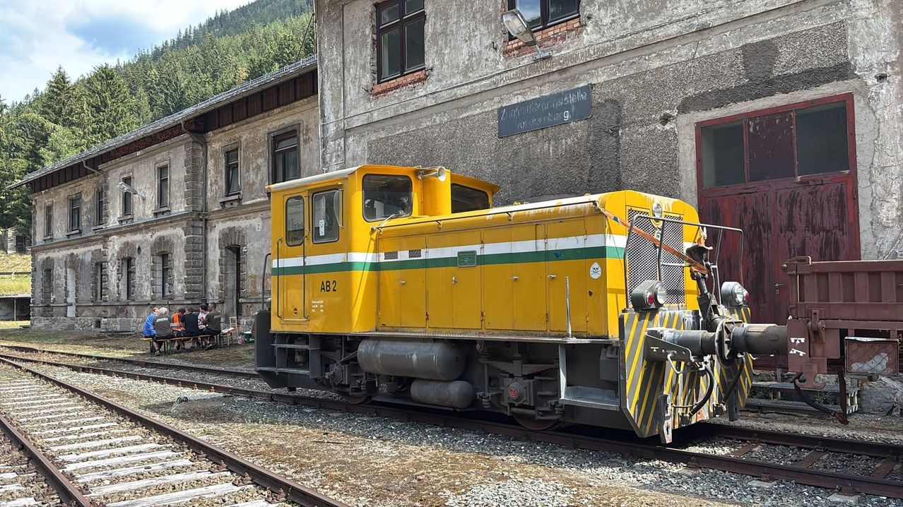 A yellow and green train engine labeled AB 2 is parked on a track in front of an old building.