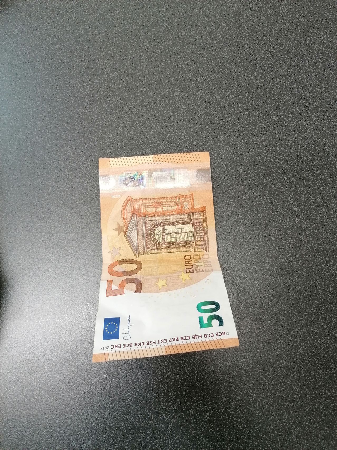 Eine gefaltete 50-Euro-Banknote auf einer strukturierten Oberfläche mit architektonischen Abbildungen und Währungsdetails.