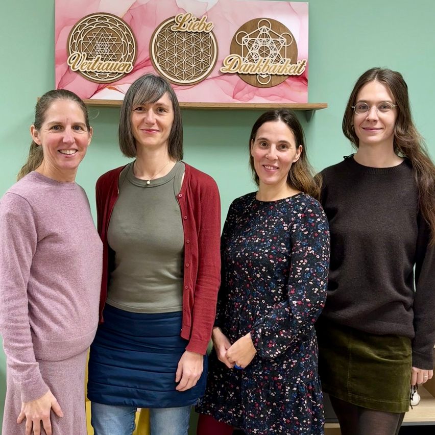 Vier Frauen stehen zusammen in einem Raum, lächeln und posieren für ein Foto vor einer Wand mit dekorativen Schildern.