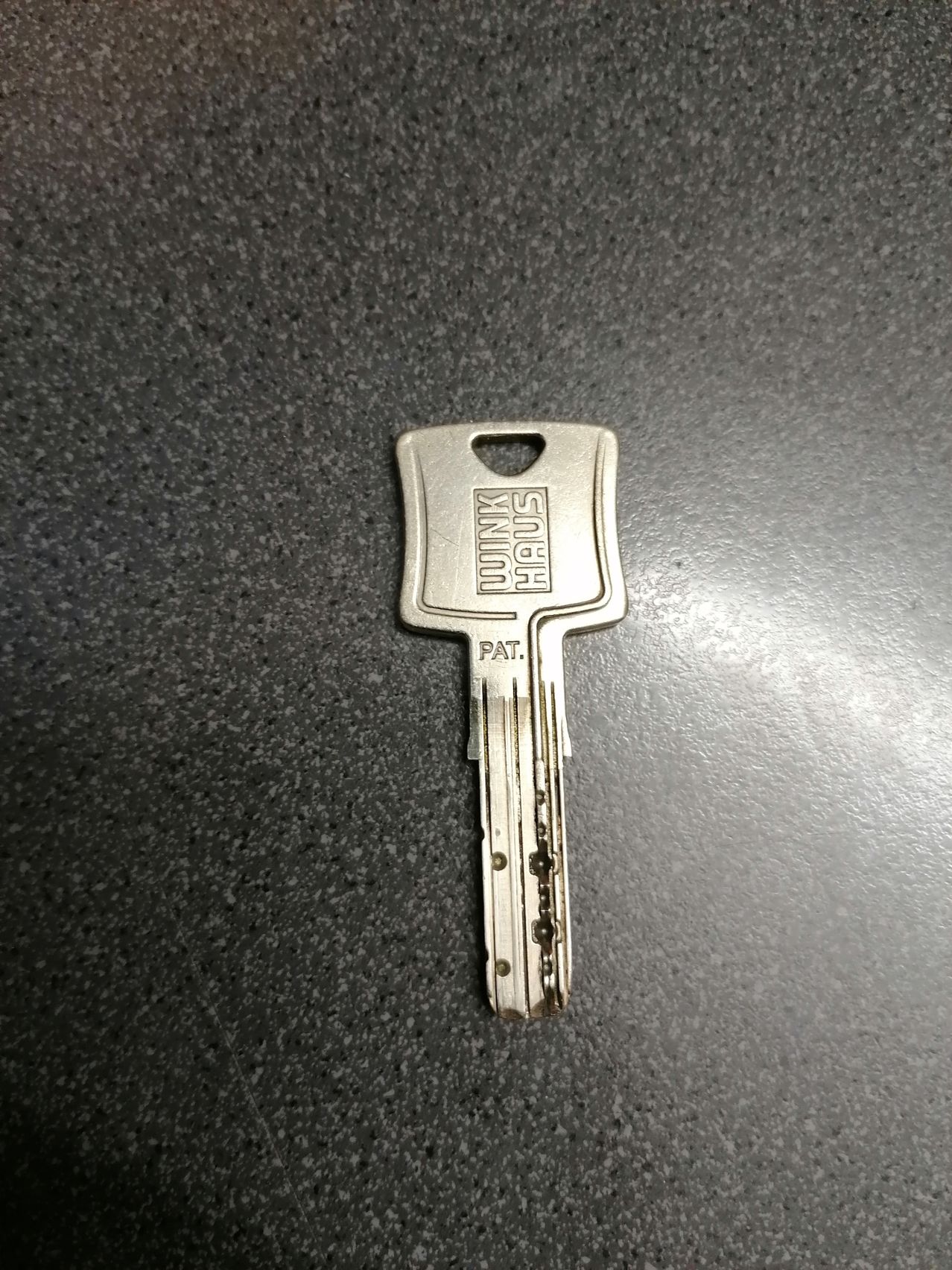Ein silberner Schlüssel mit 'MINTUM HIGH' und 'PAT.' graviert, auf einer grauen Oberfläche liegend.