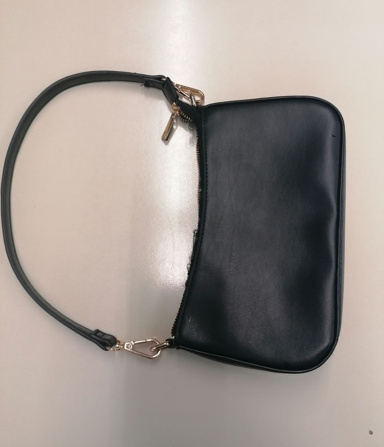 Eine schlanke schwarze Lederhandtasche mit einem einzelnen Riemen und einem goldenen Reißverschluss. Der Riemen hat eine silberne Schnalle.