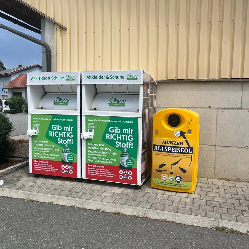Zwei grüne und weiße Spendendosen und ein gelber Speiseölbehälter auf einem Bürgersteig. Die Dosen tragen die Aufschrift Gib mir richtig Stoff! und haben Logos. Der gelbe Behälter trägt die Aufschrift Munzer Altspeiseol.