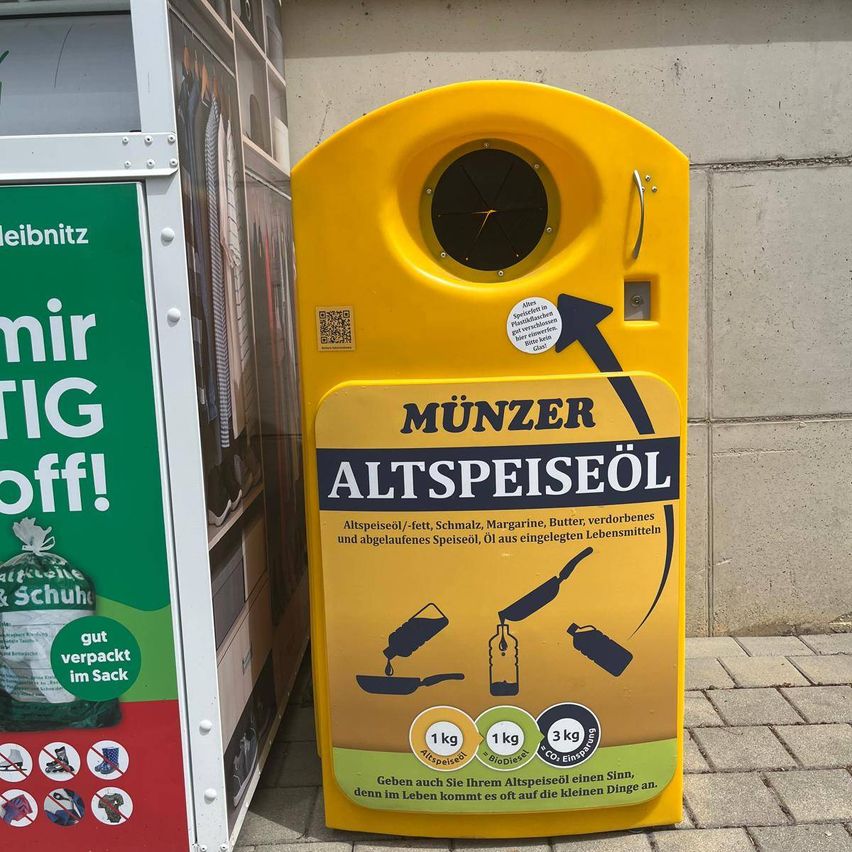 Ein gelber Abfallbehälter mit nach oben zeigendem Pfeil, beschriftet mit 'Munzer Altspeiseol'. Er hat einen QR-Code, eine Liste der akzeptierten Abfallarten und ein Gewichtslimit von 1 kg, 3 kg und CO2-Emissionen.