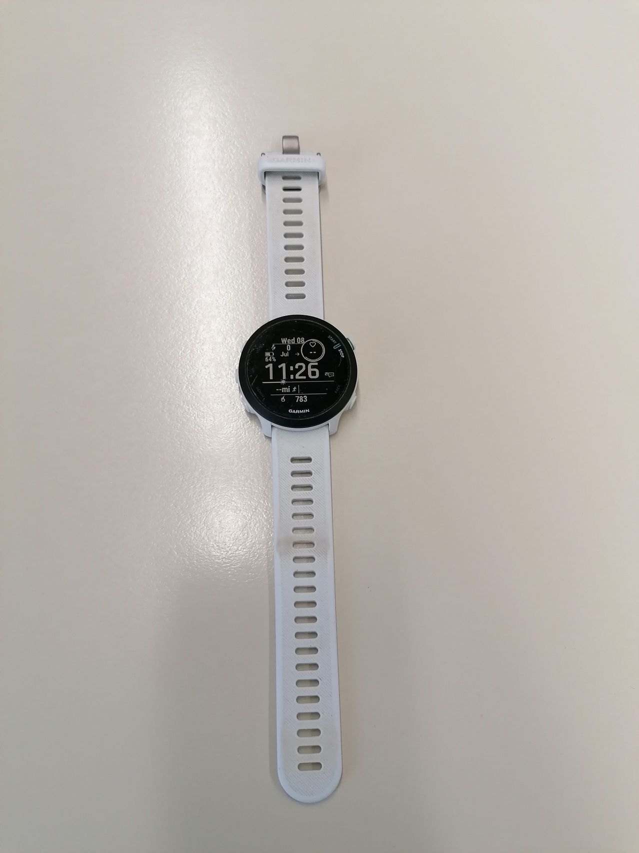 Eine weiße Smartwatch mit schwarzem kreisförmigem Gesicht, die gegen einen weißen Hintergrund gehängt. Die angezeigte Zeit ist 11:26.