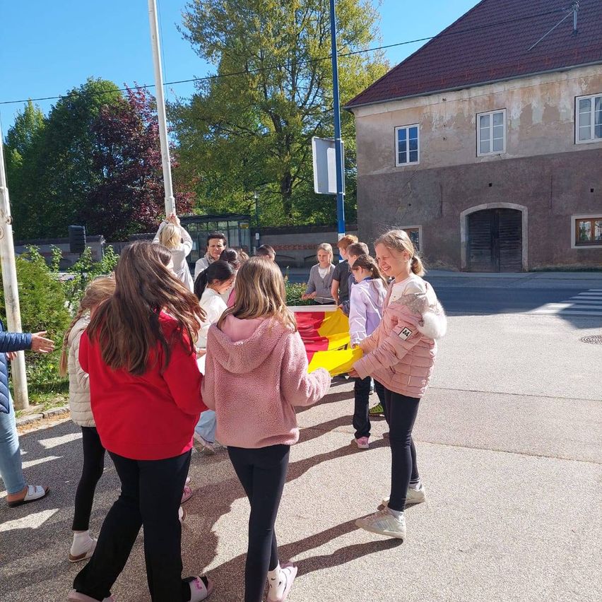 Eine Gruppe von Kindern und Erwachsenen steht auf der Straße und hält eine gelbe Flagge vor einem Gebäude.