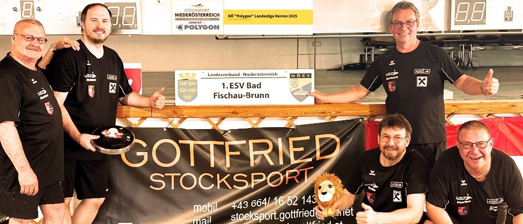 Drei Männer posieren mit einer Fahne, einem Pokal und einem Löwenmaskottchen. Sie tragen Sporttrikots und halten Pokale. Die Fahne sagt 'Gottfried Stocksport'. Hinter ihnen steht ein Schild für 'ESV Bad Fischau-Brunn'.