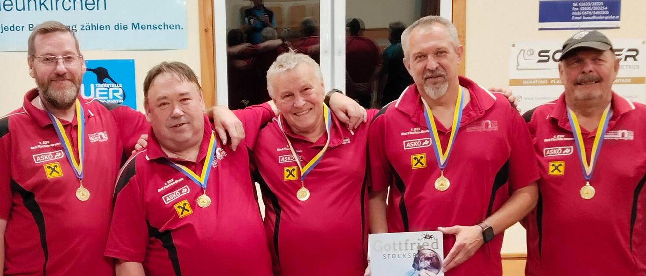 Fünf Männer in roten Trikots mit Medaillen posieren für ein Foto. Sie halten ein Papier mit einem Foto einer Frau. Hinter ihnen ist ein Banner mit den Worten "Sparkasse Neunkirchen".