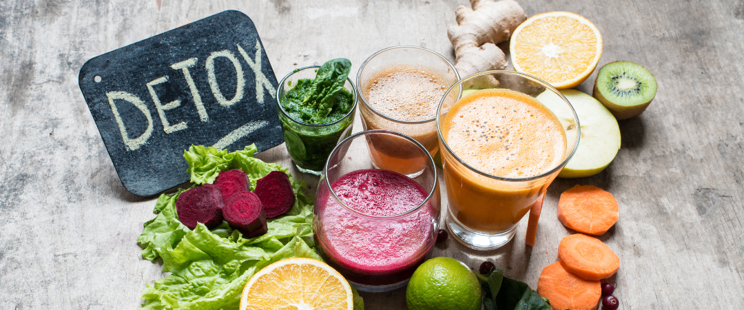 Eine Auswahl an Detox-Getränken, einschließlich Säfte und Smoothies, angeordnet mit Gemüse, Obst und Kräutern.